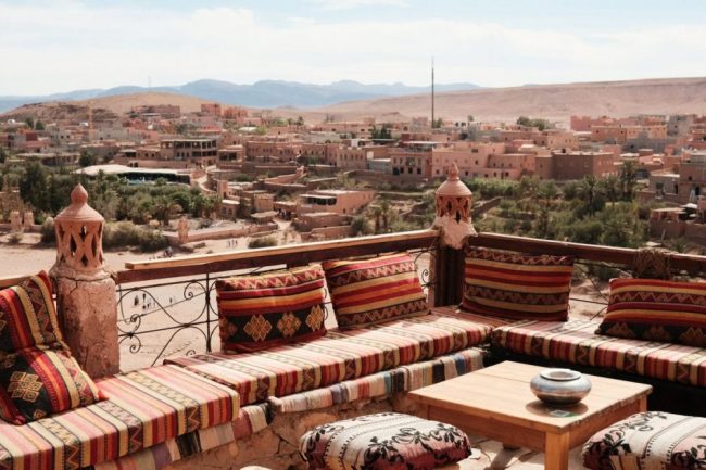 Dachterrasse mit bunten Sitzkissen und Blick &uuml;ber eine Oasenstadt in den Bergen von Marokko